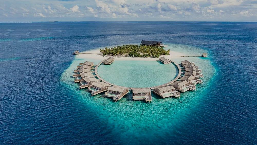 aerial view of a circular overwater resort island in a turquoise lagoon
